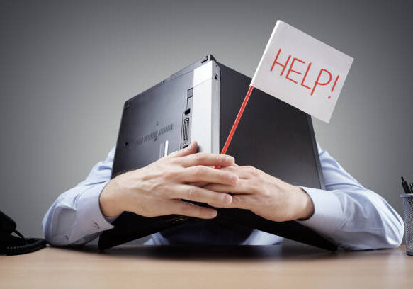 Frustrated and overworked businessman burying his head uner a laptop computer asking for help